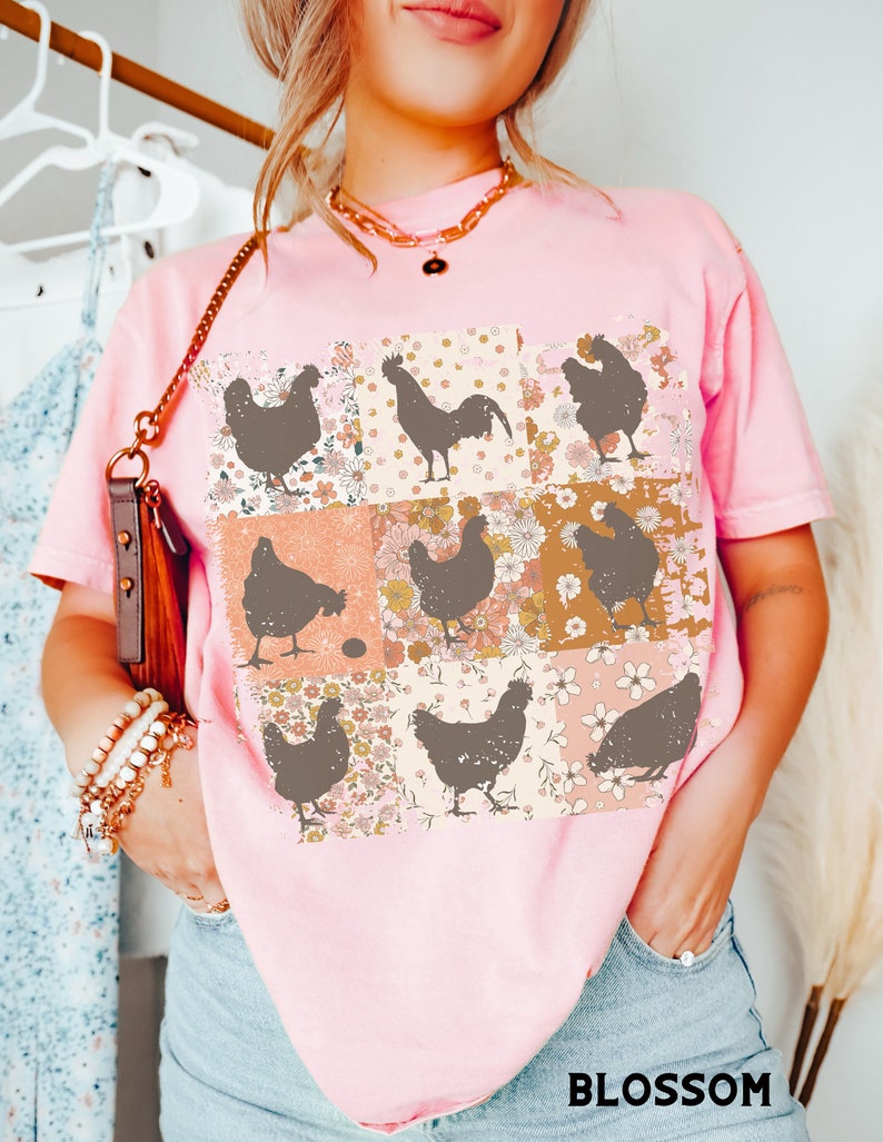 May include: Pink t-shirt with a patchwork design featuring brown silhouettes of chickens and a rooster. The patchwork design includes floral patterns in shades of pink, orange, and yellow.