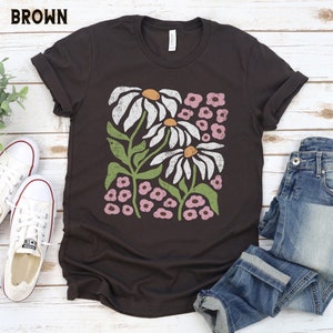 K&ouml;nnte beinhalten: Ein braunes T-Shirt mit einem Vintage-Blumenmuster mit wei&szlig;en G&auml;nsebl&uuml;mchen und rosa Bl&uuml;ten.