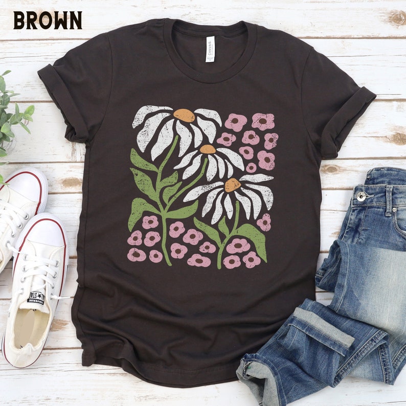 K&ouml;nnte beinhalten: Ein braunes T-Shirt mit einem Vintage-Blumenmuster mit wei&szlig;en G&auml;nsebl&uuml;mchen und rosa Bl&uuml;ten.