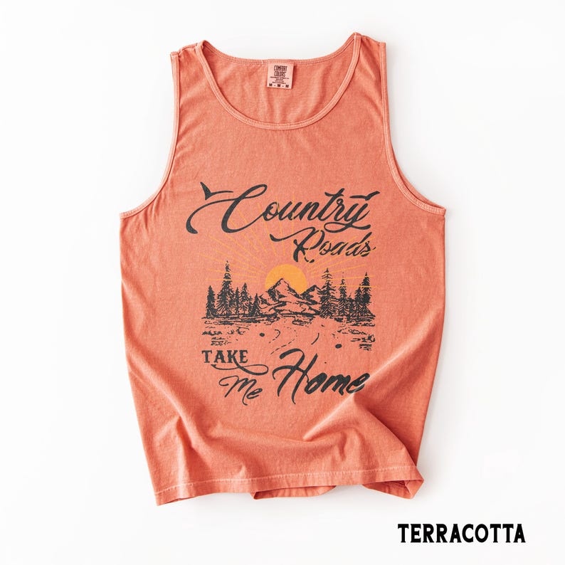 K&ouml;nnte beinhalten: Terracottafarbenes Tanktop mit dem Aufdruck "Country Roads Take Me Home". Das Design zeigt eine Berglandschaft mit B&auml;umen und einer untergehenden Sonne. Das Tanktop ist &auml;rmellos und hat einen runden Halsausschnitt. Unten steht das Wort "TERRACOTTA".