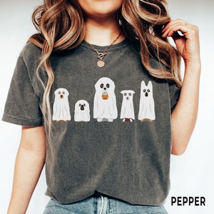 May include: A dark gray t-shirt with a graphic of five dogs dressed as ghosts for Halloween. The dogs are wearing white sheets with faces peeking out. One dog is holding a small orange pumpkin. The text "PEPPER" is printed on the bottom right corner of the shirt.