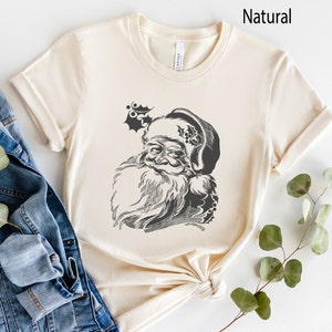 May include: A cream coloured t-shirt with a black and white illustration of Santa Claus's face. The illustration is on the front of the shirt.