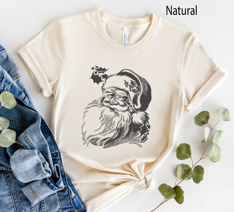 May include: A cream coloured t-shirt with a black and white illustration of Santa Claus's face. The illustration is on the front of the shirt.