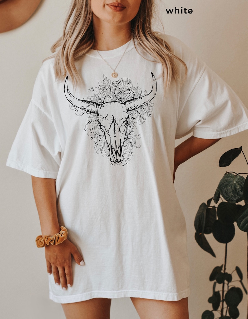 K&ouml;nnte beinhalten: Wei&szlig;es Oversize-T-Shirt mit einem schwarz-wei&szlig;en Grafikdruck eines Bullensch&auml;dels mit floralen Details.