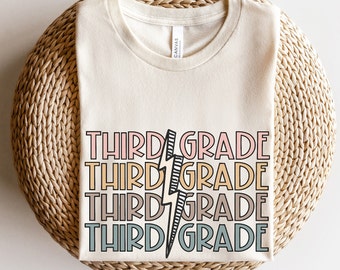 May include: A beige t-shirt with the text "THIRD GRADE" repeated four times in different colors and a black lightning bolt graphic.