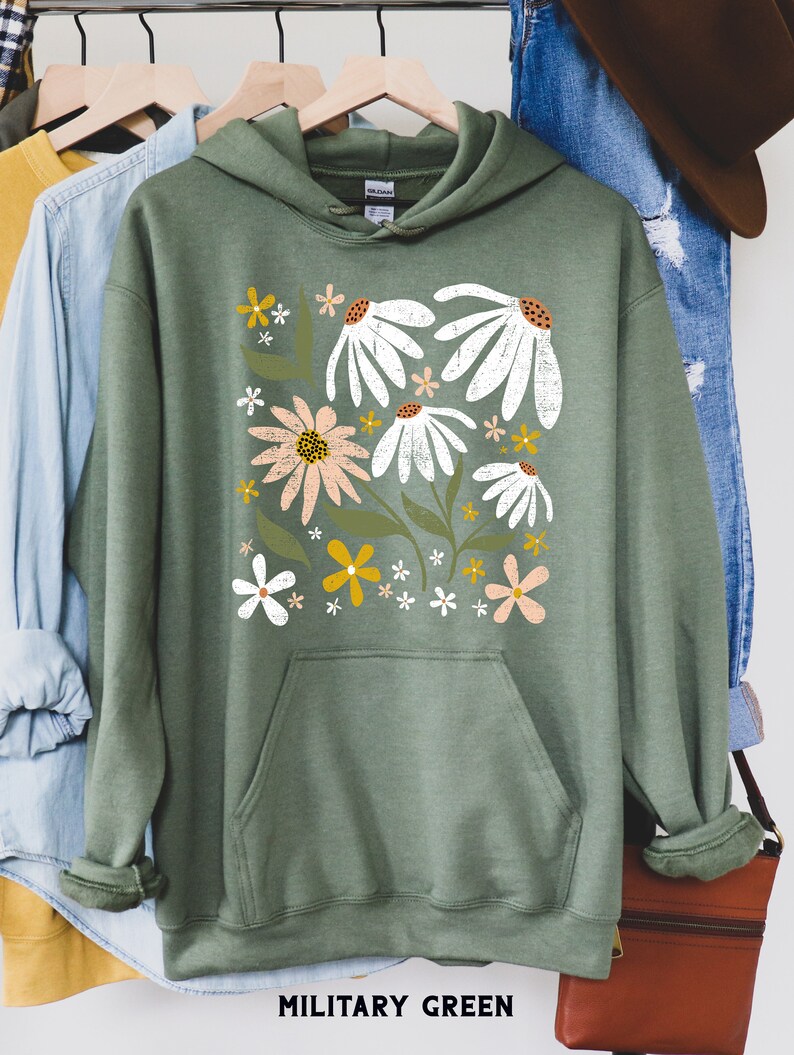 K&ouml;nnte beinhalten: Ein gr&uuml;ner Kapuzenpullover mit einem Blumendruck mit wei&szlig;en, rosa und gelben Blumen. Der Text "MILITARY GREEN" ist unter dem Bild gedruckt.