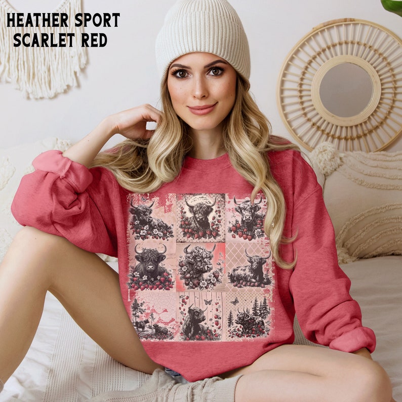May include: A heather red sweatshirt with a graphic print of a patchwork design featuring multiple images of Highland cows with flowers and butterflies. The text "HEATHER SPORT SCARLET RED" is visible at the top of the image.