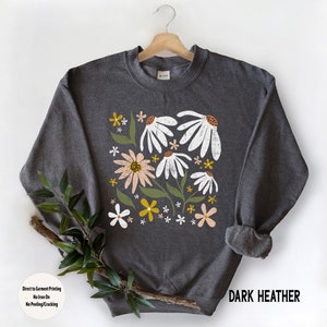 K&ouml;nnte beinhalten: Dunkelgrauer Sweatshirt mit einem Blumendruck mit wei&szlig;en, rosa und gelben Blumen. Der Text "Direct to Garment Printing No Iron On No Peeling/Cracking" und "DARK HEATHER" ist auf dem Sweatshirt aufgedruckt.