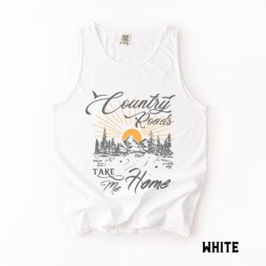 K&ouml;nnte beinhalten: Wei&szlig;es Tanktop mit dem Text "Country Roads Take Me Home" in grauer Schrift. Die Grafik zeigt eine Berglandschaft mit Sonne und B&auml;umen. Das Wort "WHITE" ist unten rechts aufgedruckt.