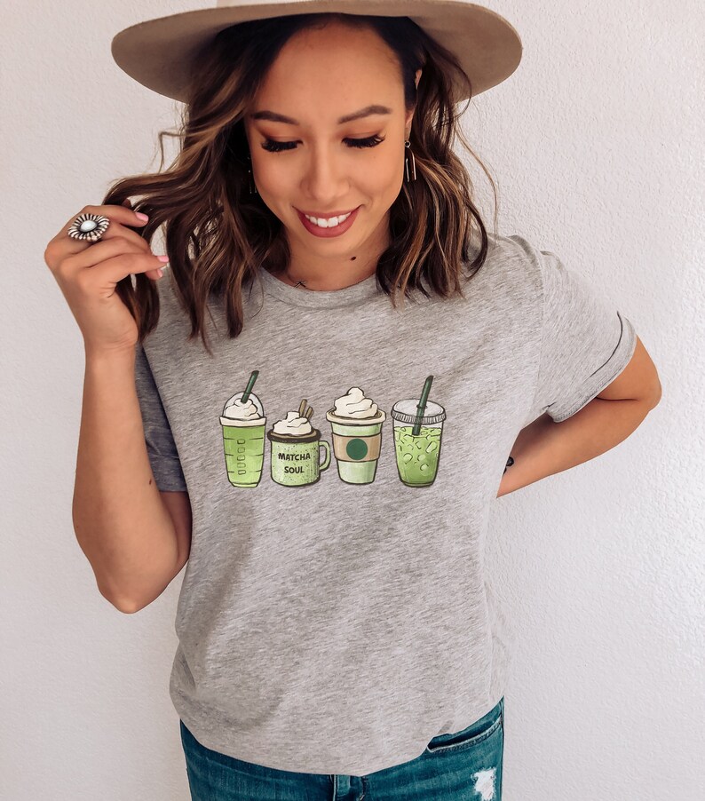 May include: A gray t-shirt with a graphic of four green drinks. The drinks are labeled "Matcha Soul" and "Green Tea".