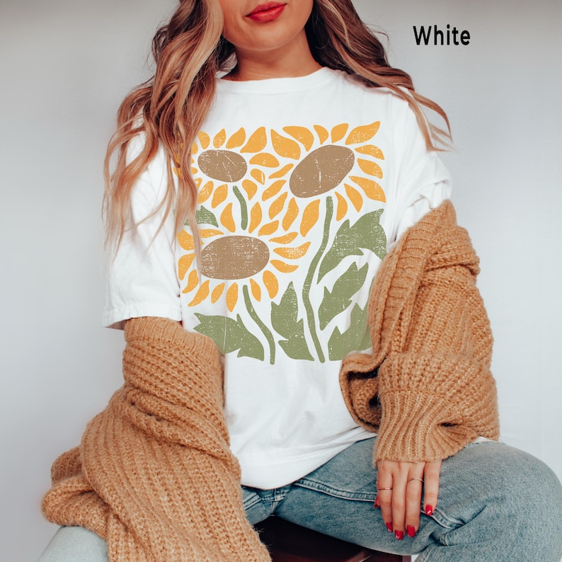 May include: White t-shirt with a graphic print of three stylized sunflowers in yellow, brown, and green.