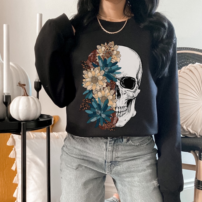 May include: Black sweatshirt with a white skull graphic and colorful floral design. The skull is partially covered by the flowers, creating a unique and stylish look.