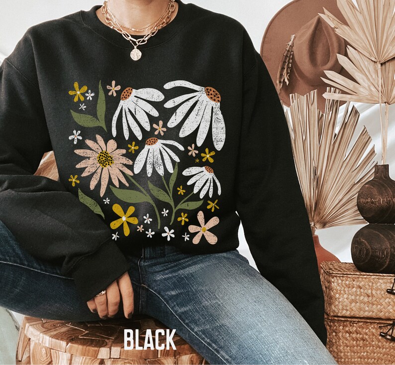 K&ouml;nnte beinhalten: Schwarzer Pullover mit einem Blumendruck mit wei&szlig;en, rosa und gelben Blumen auf schwarzem Hintergrund. Der Pullover hat einen Rundhalsausschnitt und lange &Auml;rmel.
