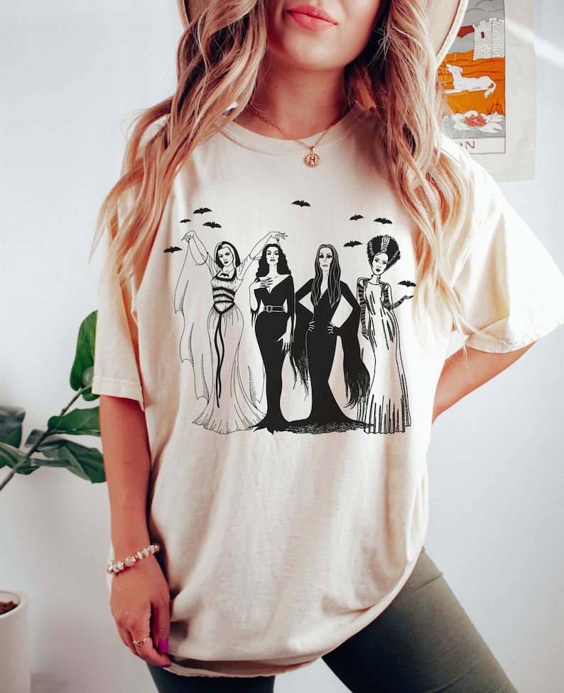 K&ouml;nnte beinhalten: Ein wei&szlig;es T-Shirt mit einem schwarz-wei&szlig;en Grafikdruck von vier Frauen in Vintage-Kleidern. Die Frauen stehen in einer Reihe und haben langes Haar. Die Grafik enth&auml;lt Flederm&auml;use, die &uuml;ber den Frauen fliegen.