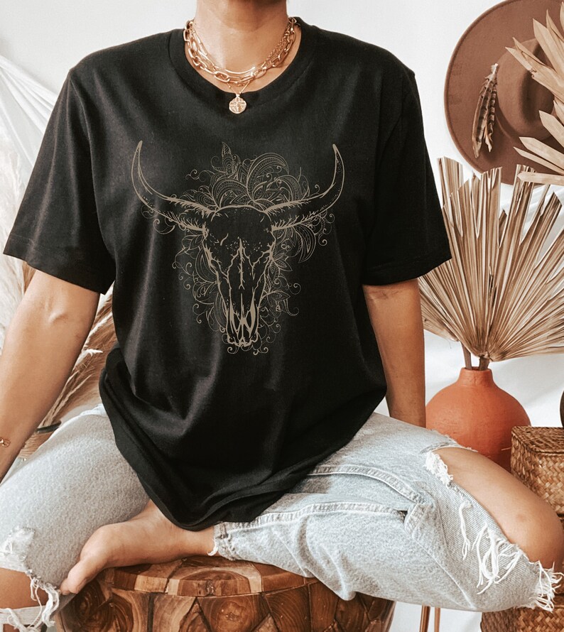 Peut inclure: T-shirt noir avec un contour dor&eacute; d'un cr&acirc;ne de taureau avec des d&eacute;tails floraux.