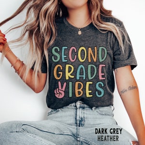 May include: Dark grey heather t-shirt with the text "Second Grade Vibes" in colorful letters with polka dots. The text is in a retro style font with a peace sign graphic.