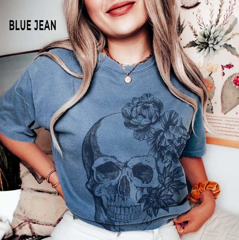 May include: Blue jean short-sleeved t-shirt featuring a skull design with floral accents. The graphic is in dark blue against the light blue shirt. The text "BLUE JEAN" is printed in the upper left corner.