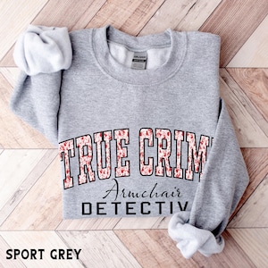 Può includere: Una felpa girocollo grigio sport con la scritta TRUE CRIME in un motivo a schizzi rosso e bianco, con le parole Armchair DETECTIVE stampate in nero sottostanti. Il capo presenta maniche lunghe e colletto, polsini e orlo a costine.