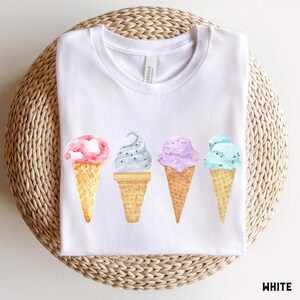 May include: White t-shirt with a graphic of four ice cream cones in different flavors: pink, gray, purple, and blue. The text "Canvas" is visible on the shirt.