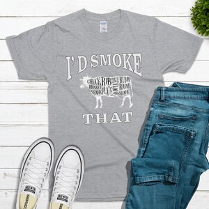 Puede incluir: Una camiseta gris con el texto "I'd Smoke That" impreso en ella. El texto est&aacute; en blanco, en negrita. Debajo del texto hay una imagen estilizada de una vaca, con las diferentes partes de la carne etiquetadas.