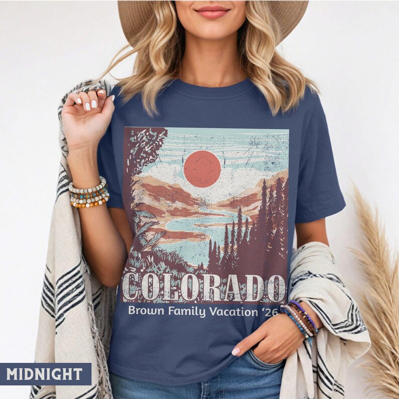 May include: Midnight blue t-shirt featuring a Colorado landscape design with a red sun, mountains, and trees. The word "COLORADO" is printed in white, with "Brown Family Vacation '26" below. The shirt is a crew neck.
