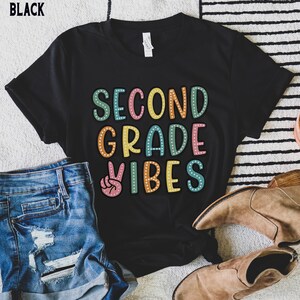 May include: Black t-shirt with the text "Second Grade Vibes" in colorful letters with a peace sign graphic.
