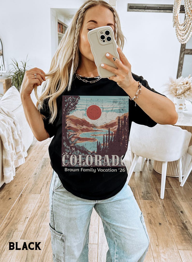 May include: Black t-shirt featuring a Colorado landscape design with a red sun, mountains, and trees. The text "COLORADO" and "Brown Family Vacation '26" are printed below the graphic. The shirt is a classic crew neck.