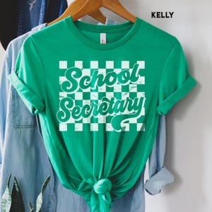 Peut inclure: T-shirt vert avec un fond &agrave; carreaux blancs et le texte "School Secretary" dans une police r&eacute;tro.