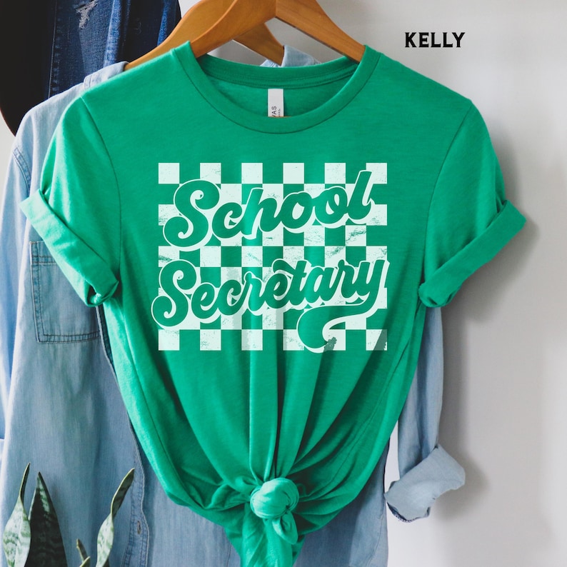 Peut inclure: T-shirt vert avec un fond &agrave; carreaux blancs et le texte "School Secretary" dans une police r&eacute;tro.