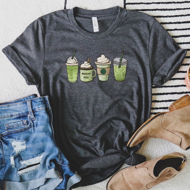 May include: A dark gray t-shirt with a graphic of four different green drinks. The drinks are labeled "Matcha Soul".