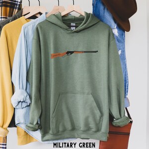 May include: A green hooded sweatshirt with a pocket on the front. The sweatshirt has a graphic of a rifle on the front. The text "MILITARY GREEN" is printed on the bottom of the sweatshirt.
