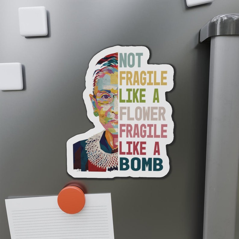 May include: A colorful illustration of Ruth Bader Ginsburg with the text "Not Fragile Like A Flower Fragile Like A Bomb" in a vintage style.