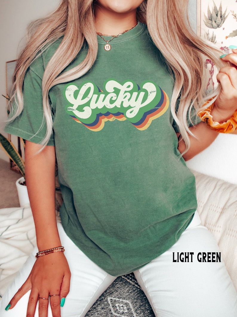 May include: A light green t-shirt with a retro-style graphic that says "Lucky" in a rainbow of colors.