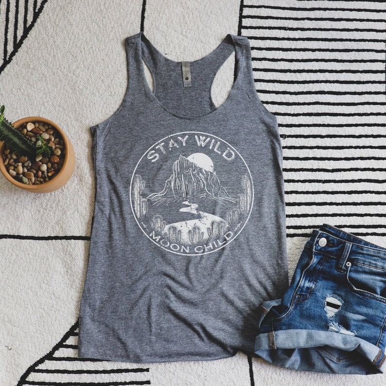 May include: Gray tank top with a white graphic of a mountain range, a moon, and cacti. The graphic is in a circle with the text "Stay Wild Moon Child".