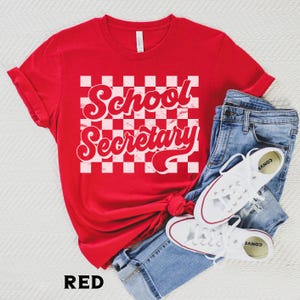 Peut inclure: T-shirt rouge avec un fond &agrave; carreaux blancs et le texte "School Secretary" dans une police r&eacute;tro.