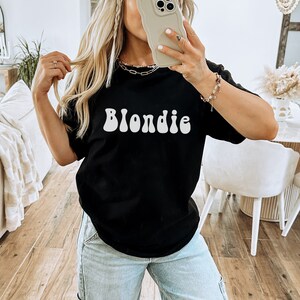 以下が含まれることがあります： レトロなフォントで白く印刷された「Blondie」という単語が書かれた黒いTシャツです。