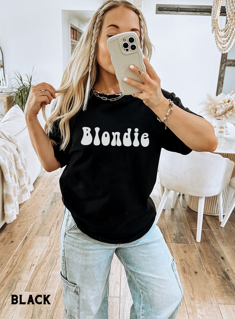 以下が含まれることがあります： レトロなフォントで白く印刷された「Blondie」という単語が書かれた黒いTシャツです。