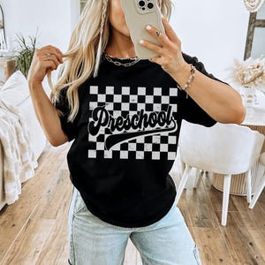 Pu&ograve; includere: T-shirt nera con motivo a scacchi e la scritta "Preschool" in corsivo. La maglietta &egrave; a girocollo. La parola "BLACK" &egrave; stampata in basso nell'immagine.
