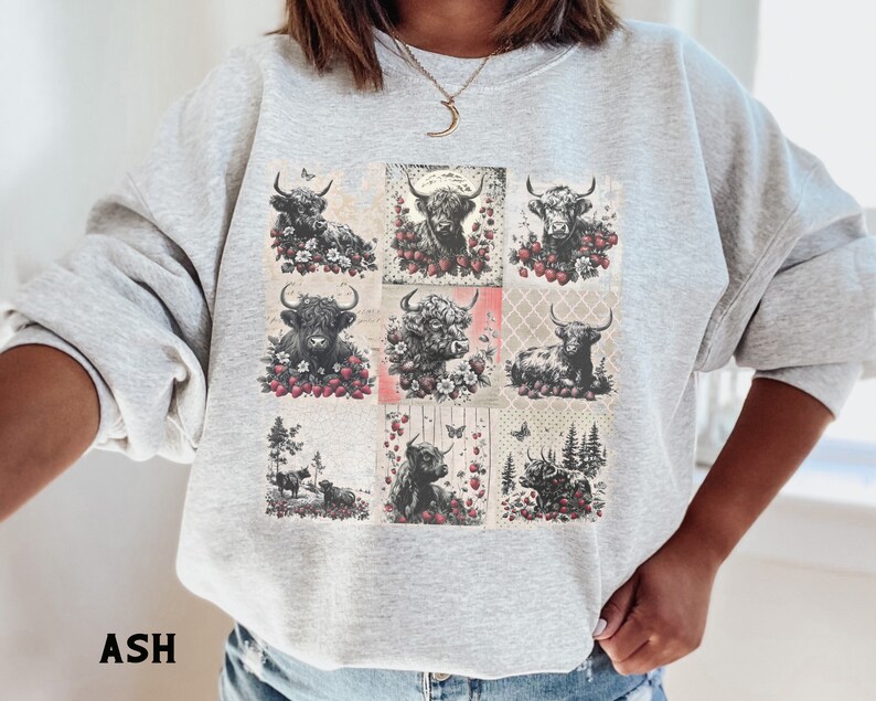 May include: A gray sweatshirt with a patchwork design featuring black and white illustrations of Highland cattle with red berries and butterflies. The text "ASH" is printed on the bottom left corner of the image.