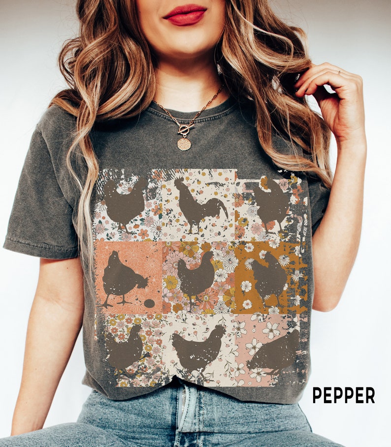May include: A charcoal gray t-shirt with a vintage-inspired design featuring a rooster and hens in a patchwork pattern with floral accents. The text "PEPPER" is visible in the bottom right corner.