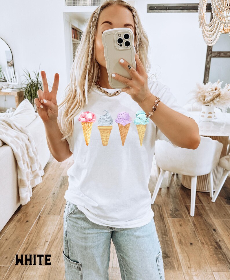 May include: White t-shirt with a graphic of four ice cream cones in different colors. The ice cream cones are in a row, with the pink ice cream cone on the left and the blue ice cream cone on the right.
