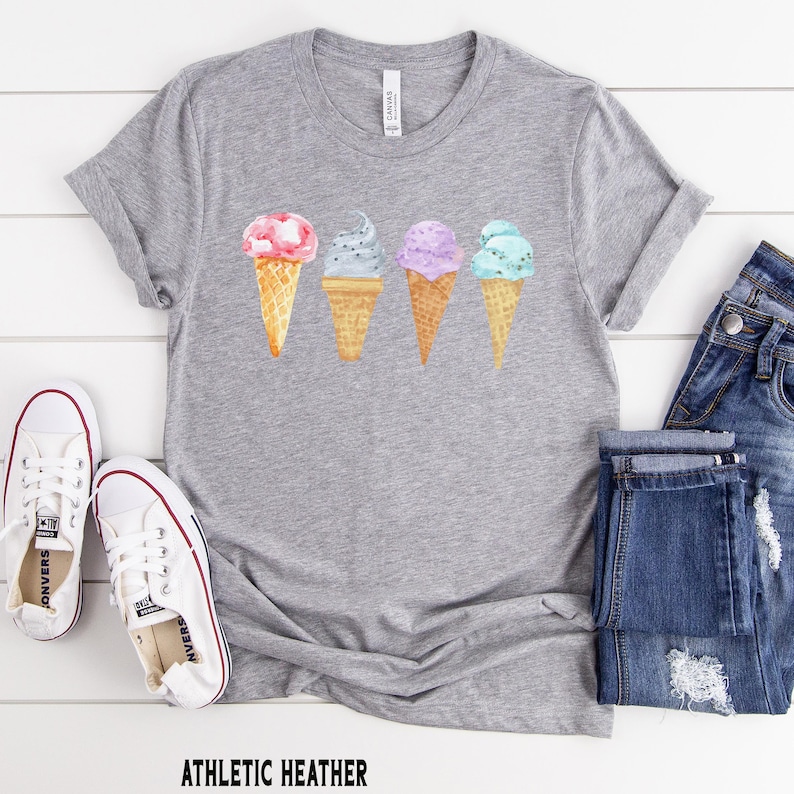 May include: A gray t-shirt with a graphic of four ice cream cones in different colors. The ice cream cones are pink, gray, purple, and blue.