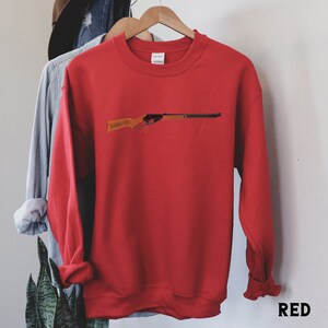 May include: Red sweatshirt with a black and brown toy rifle graphic on the front. The sweatshirt has a crew neck and long sleeves.