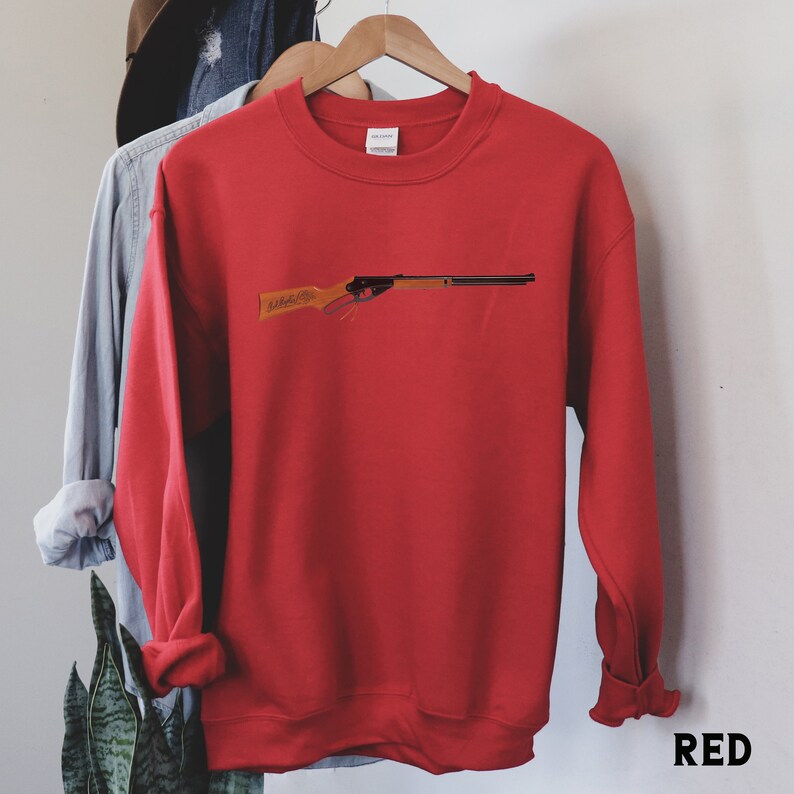 May include: Red sweatshirt with a black and brown toy rifle graphic on the front. The sweatshirt has a crew neck and long sleeves.