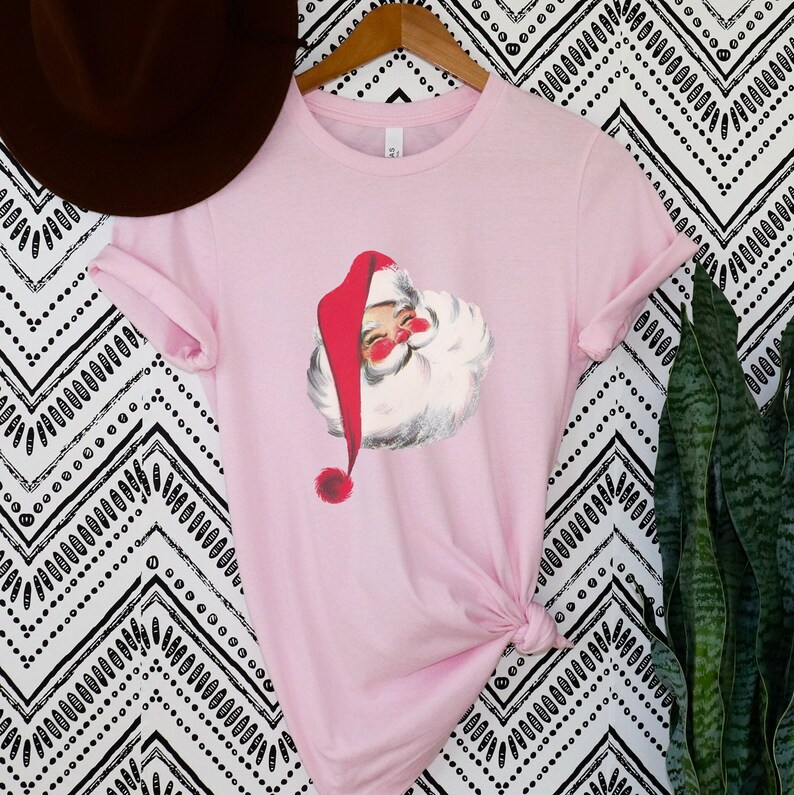 May include: A pink t-shirt with a vintage illustration of Santa Claus on the front. The illustration is in red, white, and black.
