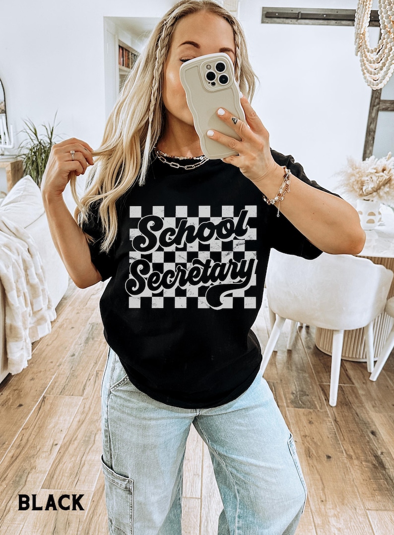 Peut inclure: T-shirt noir avec un fond &agrave; carreaux blancs et le texte "School Secretary" dans une police r&eacute;tro.
