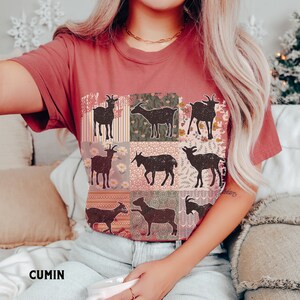 May include: A red t-shirt with a patchwork design featuring nine black silhouettes of goats. Each goat is surrounded by a different floral pattern.