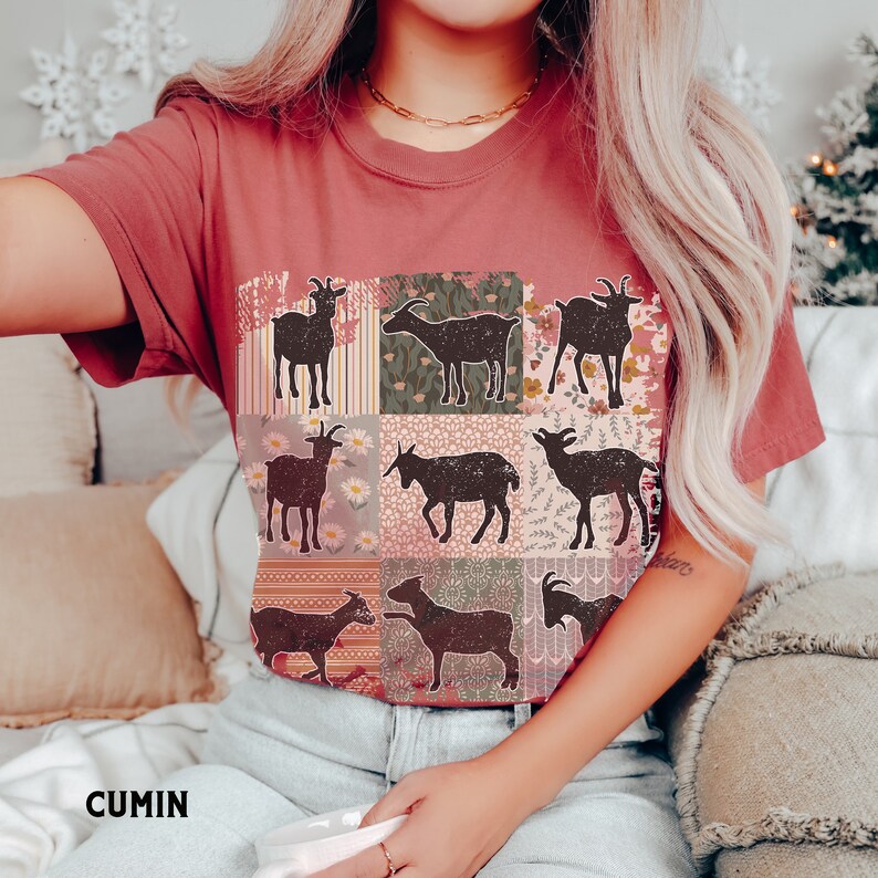 May include: A red t-shirt with a patchwork design featuring nine black silhouettes of goats. Each goat is surrounded by a different floral pattern.