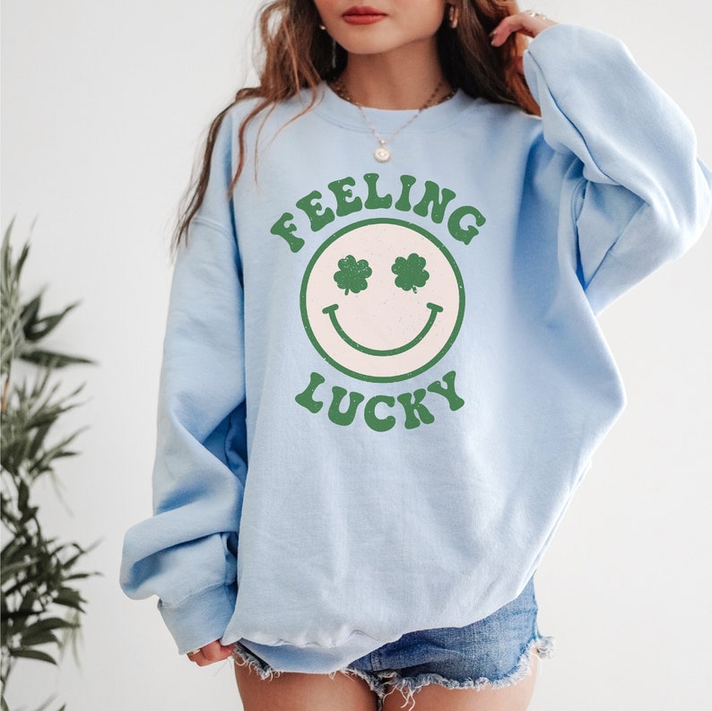May include: Light blue sweatshirt with a graphic of a smiling face with shamrock eyes and the text "Feeling Lucky".