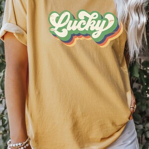 May include: A mustard yellow t-shirt with a retro-style graphic that says "Lucky" in green, red, blue, and orange.